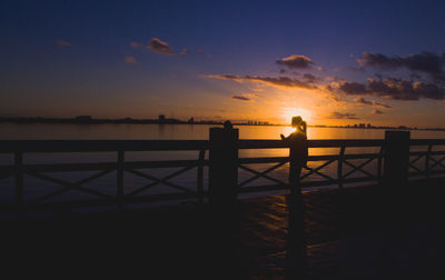 Silhouette people standing by railing against sky during sunset