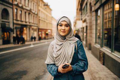 Portrait of young woman standing on street in city