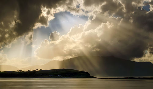 Sunlight streaming through clouds over sea during sunset