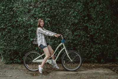 Full length portrait of woman with bicycle against plants