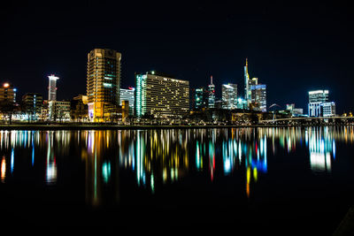 Illuminated buildings by river against sky at night