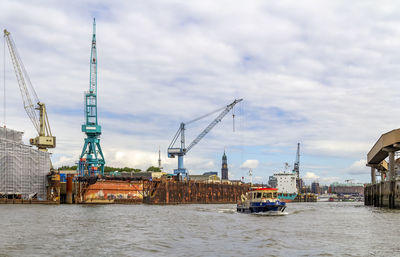 Cranes at harbor against sky