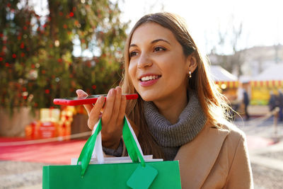 Close-up of beautiful girl carrying shopping bags and recording voice message for christams holidays