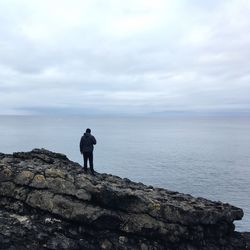 Man standing on rock by sea against sky