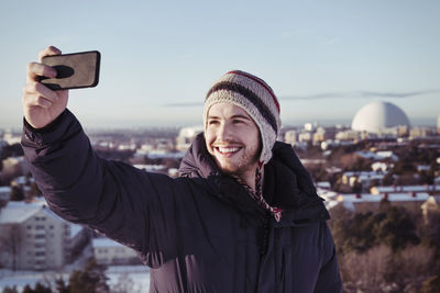 Smiling young man clicking selfie through smart phone during winter