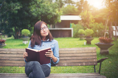 Thoughtful young woman looking away while holding book on park bench
