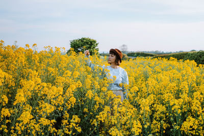 Woman standing by yellow flowers on field against sky