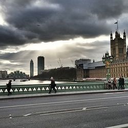 People walking in city against cloudy sky