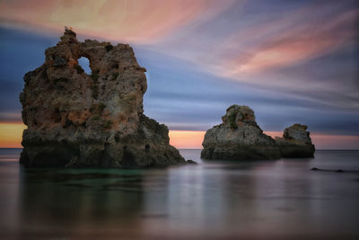 Rock formation in sea against sky during sunset