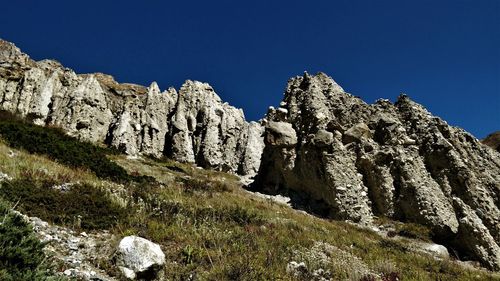 Low angle view of rocks against clear blue sky