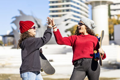 Teenage girls giving high-five while standing in city