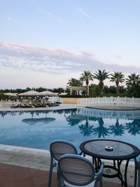 Chairs by swimming pool against sky