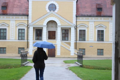 Rear view of woman with umbrella walking in building during rainy season