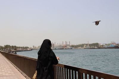 Rear view of woman standing on pier against clear sky