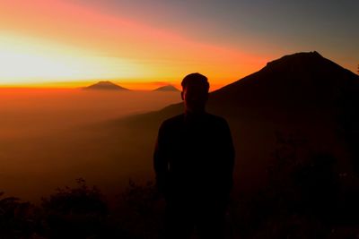 Rear view of silhouette woman standing on mountain against sky during sunset