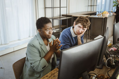 Tensed multiracial male and female programmers looking at computer monitor in creative office