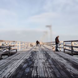 People on pier at sea against sky