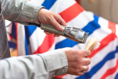 Cropped hands of barber cleaning electric razor in shop