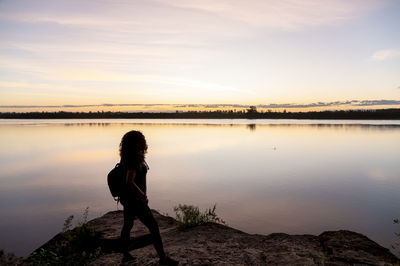 Full length of woman standing at lakeshore during sunset