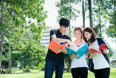 Low angle view of friends discussing while standing against trees at park