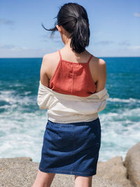 Rear view of woman wearing tank top while standing on beach against sea