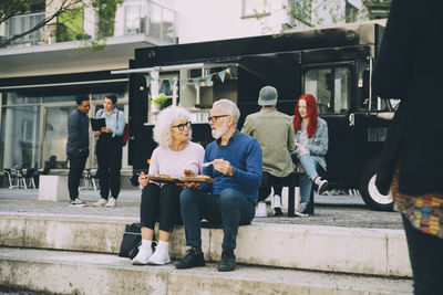 Senior male and female customers enjoying meal against food truck in city
