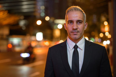 Portrait of mature man standing in illuminated city at night