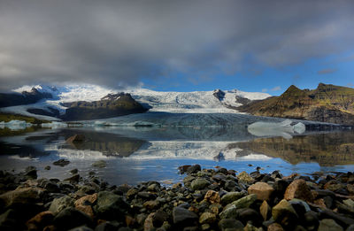 Scenic view of lagoon by mountain against cloudy sky