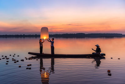 Silhouette wooden posts in lake against sky during sunset