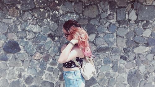 Side view of redhead young woman standing by stone wall