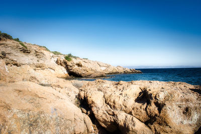 Rock formation in sea against clear blue sky