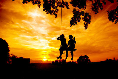 Silhouette people on street against sky during sunset