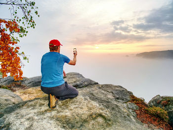 Rear view of man on rock against sky during sunset