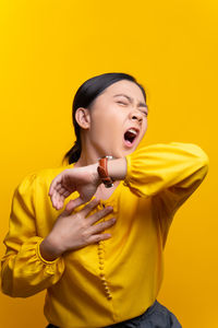 Beautiful young woman standing against yellow background