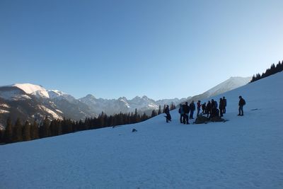 People on snow covered mountain against clear blue sky