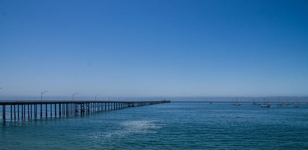 Pier over sea against clear blue sky