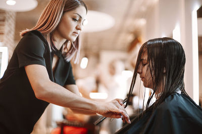 Hairdresser cutting hair of girl at salon