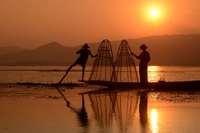 Silhouette men fishing in lake at sunset