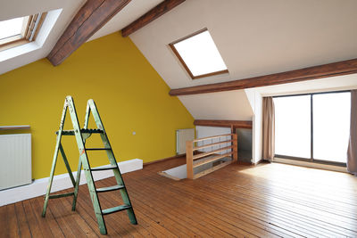 Green ladder against yellow wall in a renovated interior attic.