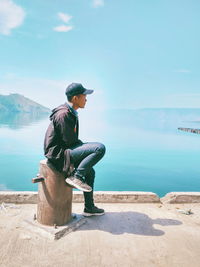 Side view of young man looking at sea against sky