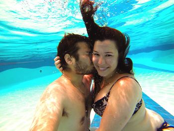 Shirtless man kissing happy beautiful woman in swimming pool