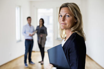 Portrait of confident female real estate agent with couple standing in background at home