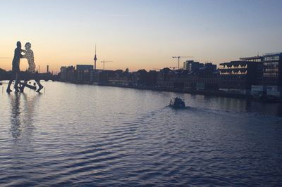 Silhouette buildings by river against sky during sunset