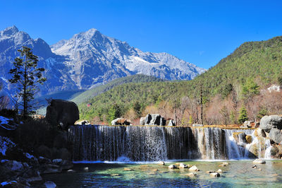 Scenic view of waterfall by mountains against sky