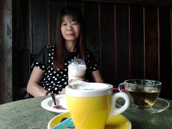 Portrait of woman having drink while sitting at table against wall