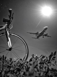 Low angle view of bicycle with airplane flying against sky on sunny day