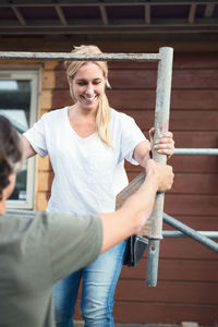 Smiling woman with man working on scaffolding outside house being renovated