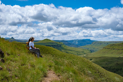 Side view of woman sitting on ridge against sky