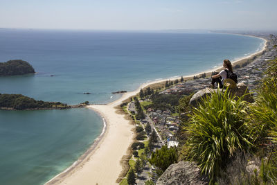 Female backpacker, sitted on top of mount maunganui, looking at view