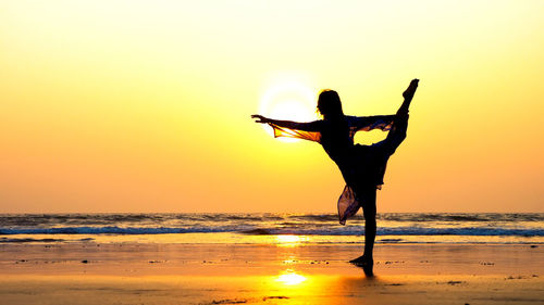 Side view of silhouette woman practicing yoga at beach during sunset